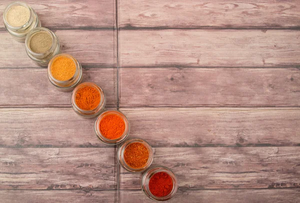 Hot and spicy spices powder, cayenne powder, chilly powder, peppercorn powder, paprika powder, black pepper and white pepper powder in small mason jar over wooden background