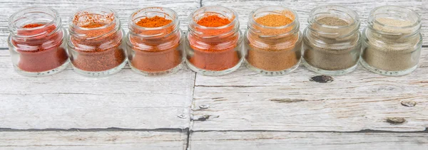 Hot and spicy spices powder, cayenne powder, chilly powder, peppercorn powder, paprika powder, black pepper and white pepper powder in small mason jar over wooden background