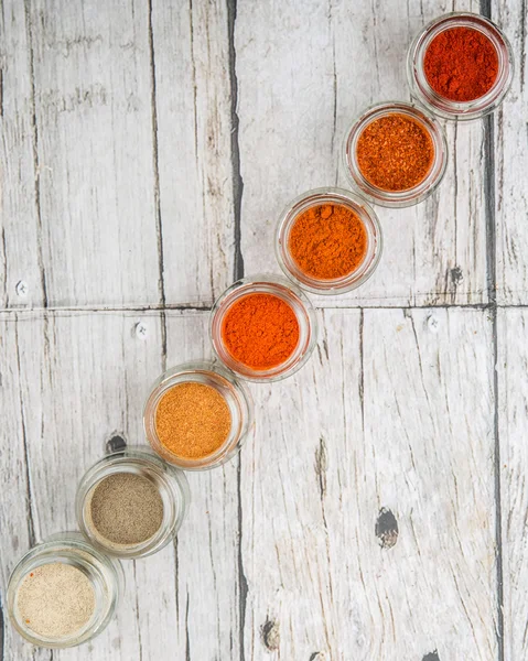 Hot and spicy spices powder, cayenne powder, chilly powder, peppercorn powder, paprika powder, black pepper and white pepper powder in small mason jar over wooden background