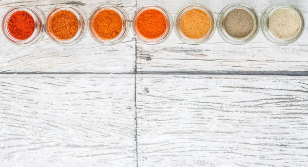 Hot and spicy spices powder, cayenne powder, chilly powder, peppercorn powder, paprika powder, black pepper and white pepper powder in small mason jar over wooden background