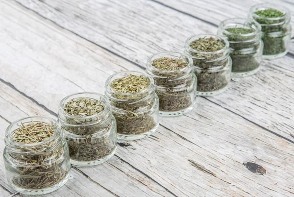 Dried parsley, estragon, marjoram, dill weed, rhyme, rosemary and basil herbs in mason jar over wooden background