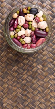 Hasır arka plan üzerinde siyah göz bezelye, mung fasulye, adzuki fasulyesi, soya fasulyesi, siyah fasulye ve kırmızı barbunya fasulyesi bir mason kavanoza fasulye mix