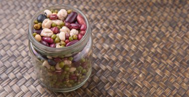 Hasır arka plan üzerinde siyah göz bezelye, mung fasulye, adzuki fasulyesi, soya fasulyesi, siyah fasulye ve kırmızı barbunya fasulyesi bir mason kavanoza fasulye mix