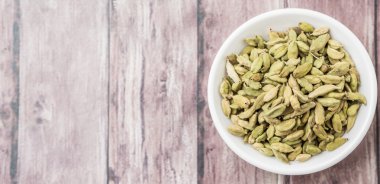 Kakule baharat yıpranmış ahşap arka plan üzerinde beyaz bir kase