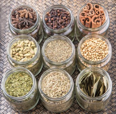 Kakule, Yıldız anason, tarçın, karanfil, kişniş tohumu baharat ve kurutulmuş defne yaprağı, maydanoz, kekik, biberiye otlar mason kavanoz hasır arka plan üzerinde
