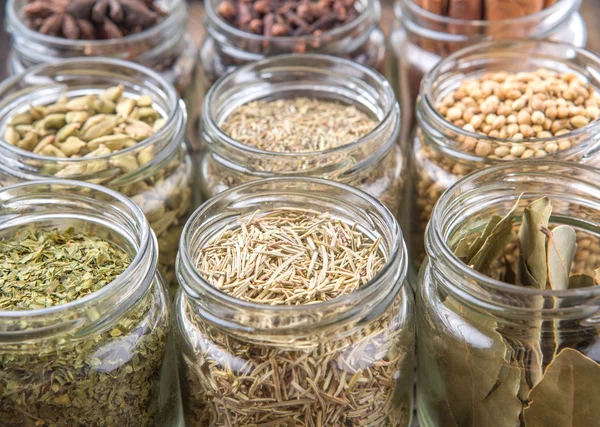 Kakule, Yıldız anason, tarçın, karanfil, kişniş tohumu baharat ve kurutulmuş defne yaprağı, maydanoz, kekik, biberiye otlar mason kavanoz hasır arka plan üzerinde