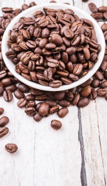 Kavrulmuş kahve çekirdekleri rustik ahşap arka plan üzerinde beyaz kase