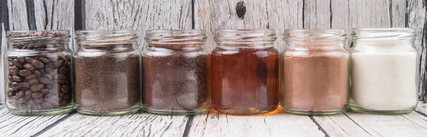 Coffee beans, coffee powder, creamer, cocoa powder, honey and processed tea leaves in a mason jar over weathered wooden background