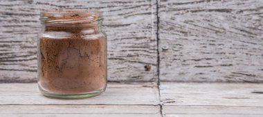 Rustik ahşap arka plan üzerinde bir mason kavanoza kahverengi saf kakao tozu