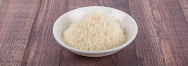 Ahşap arka plan üzerinde beyaz kase içinde rendelenmiş peynir