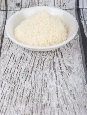 Ahşap arka plan üzerinde beyaz kase içinde rendelenmiş peynir