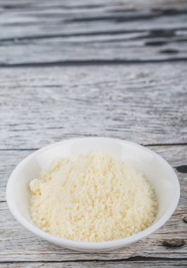 Ahşap arka plan üzerinde beyaz kase içinde rendelenmiş peynir