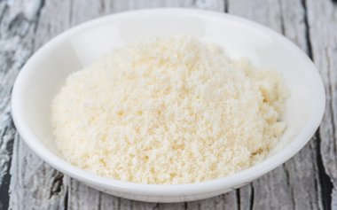 Ahşap arka plan üzerinde beyaz kase içinde rendelenmiş peynir