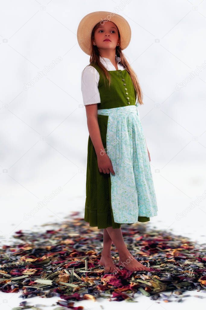 Young girl in dirndl and summer hat standing on mowed wild flowers with white background