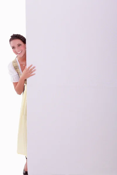 Young woman in dirndl hiding behind a wall — Stock Photo, Image