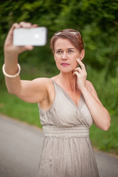 Mulher de vestido tomando auto retrato com celular — Fotografia de Stock