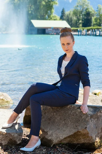 Молодая предпринимательница, сидящая на большом камне у озера — стоковое фото