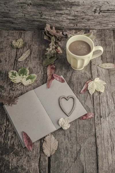 Coffee and notebook on table decorated with dried autumn leaves — Stock Photo, Image