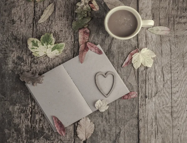 Coffee and notebook on table decorated with dried autumn leaves — Stock Photo, Image