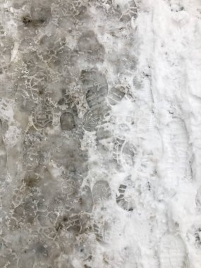 Kışın karla kaplı kaldırımda ayak izleri.