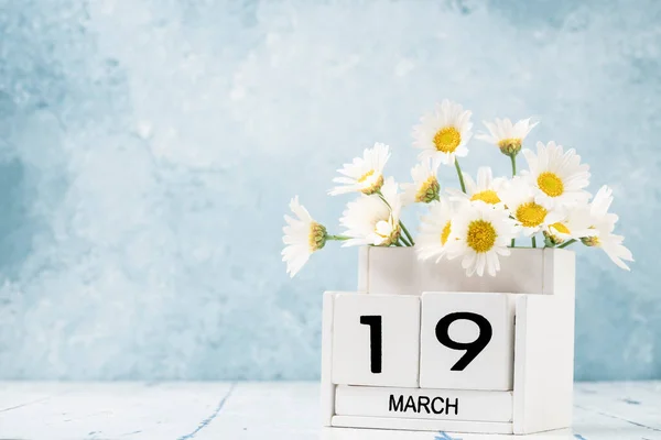 White cube calendar for march decorated with daisy flowers over blue background with copy space