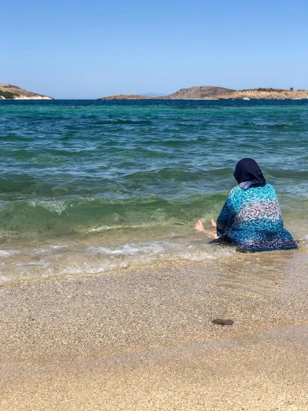 peasant muslim woman sitting in the water on the sea shore with her clothes