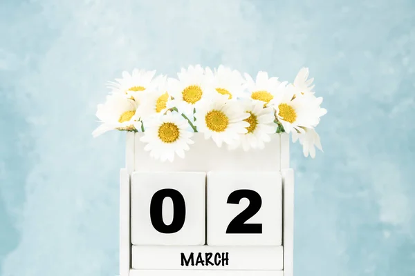 White cube calendar for March with daisy flowers over blue background with copy space