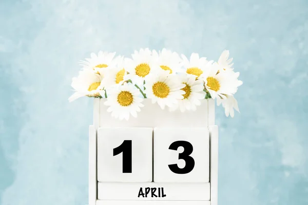 White cube calendar for April with daisy flowers over blue background with copy space