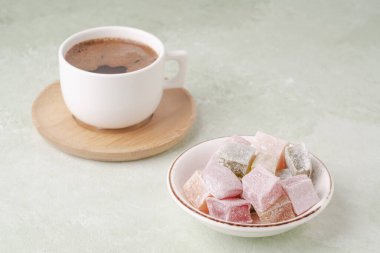 Yeşil bir masada bir fincan kahve ve renkli Türk lokumu.