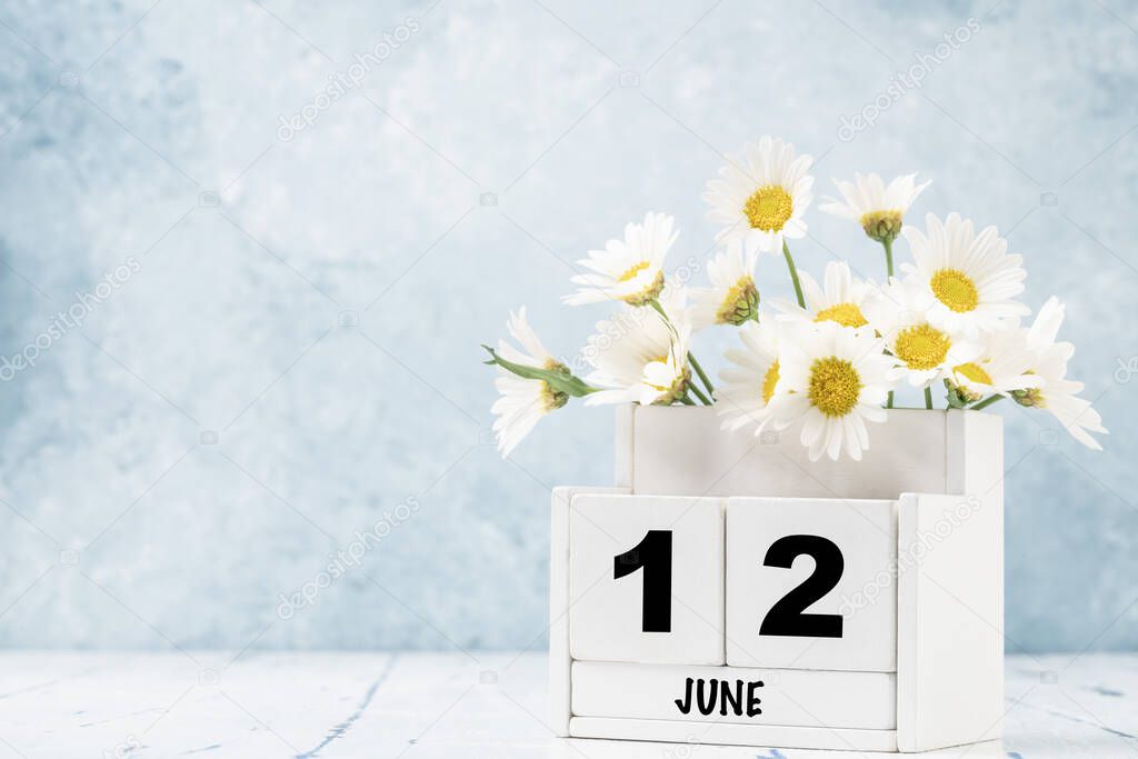 White cube calendar for June decorated with daisy flowers over blue background with copy space