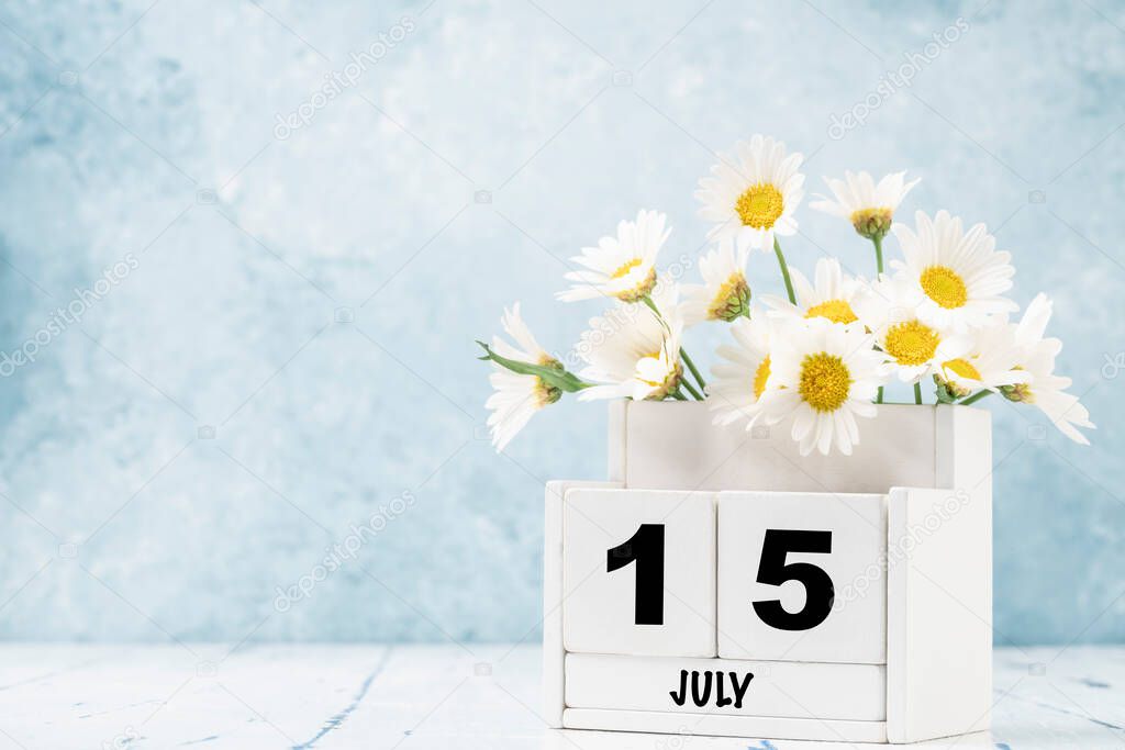 White cube calendar for July decorated with daisy flowers over blue background with copy space