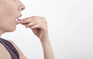 Genç bir kadın beyaz arka plan üzerinde fotokopi alanı ile hap alıyor.