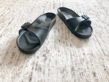 Yakın plan siyah terlikler halının üzerinde.