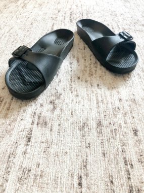 Yakın plan siyah terlikler halının üzerinde.