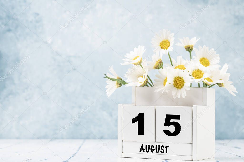 White cube calendar for August decorated with daisy flowers over blue background with copy space