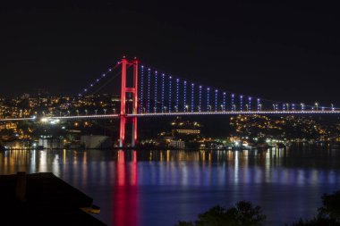 İstanbul, Türkiye 'de geceleyin denizi yansıtan ışıklı Boğaz Köprüsü