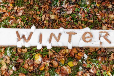 Sonbahar yapraklarının arka planında kar üzerine yazılmış bir yazı var, Winter.