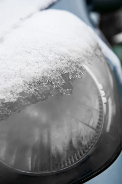 Car headlight covered with snow and ice, close-up. Automobile in winter day, snowstorm outdoors