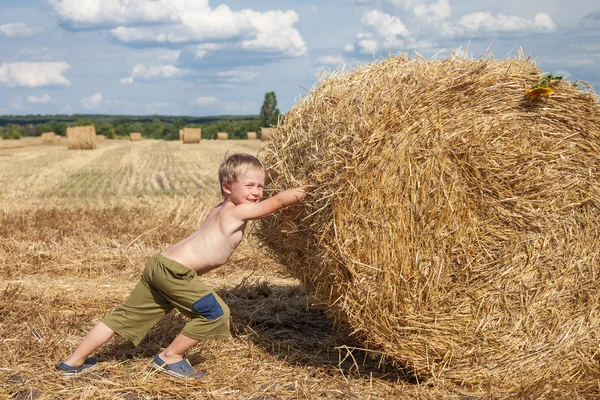 Boy pushes bale of straw — Stock Photo, Image