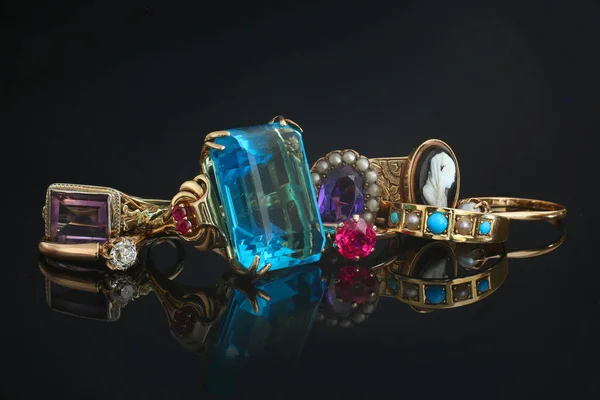 Pile of vintage rings of different color gemstones and diamonds on black reflective background