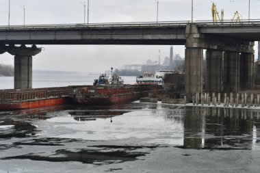 Nehir ve köprü. Köprünün altında gemiler var. Buz ve gemilerden oluşan bir manzara. Nehirdeki beton köprü. port ve gemiler