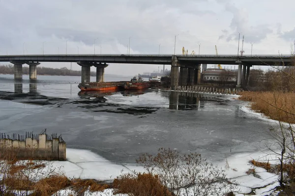 river and bridge. ships under the bridge. landscape with ice and ships. concrete bridge on the river. port and ships