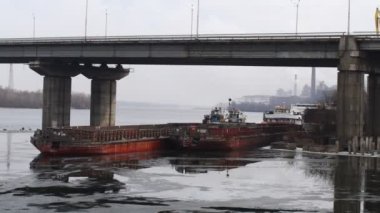 Nehir ve köprü. Köprünün altında gemiler var. Buz ve gemilerden oluşan bir manzara. Nehirdeki beton köprü. port ve gemiler