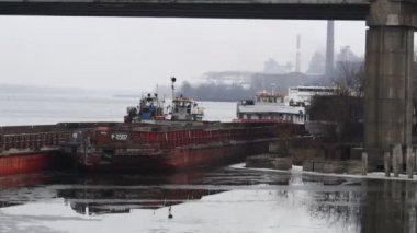 Nehir ve köprü. Köprünün altında gemiler var. Buz ve gemilerden oluşan bir manzara. Nehirdeki beton köprü. port ve gemiler
