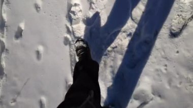 Karlı yolda yürüyen erkek ayağının en üst görüntüsü. Çizmeli adam yola çıkıyor, bembeyaz kara basıyor. Tanımlanamayan yürüyüşçü ormanda geziniyor. Kış konsepti POV Yavaş çekim Kapat