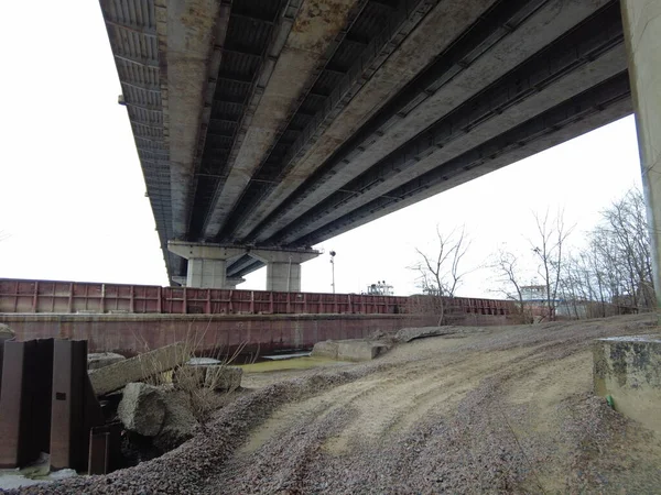 under the big bridge. Powerful iron bridge structure, View from below.A river flows under the bridge. Perspective. City architecture. The bridge on the fon of dawn. The construction of bridges.