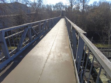 Demir köprü. Köprüden karşıya yürü. Demir zemin. Yol verin. İçeriden yaya geçidi yükselmiş. Yolun karşısına güvenli bir geçiş. Metal merdiven manzarası yere bakıyor..