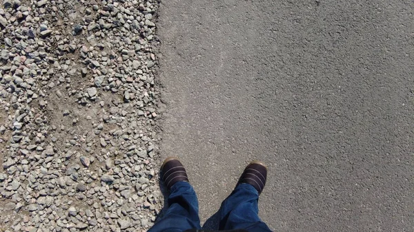 a man walks on an asphalt road. Men\'s feet on the asphalt. A man walks along the road markings