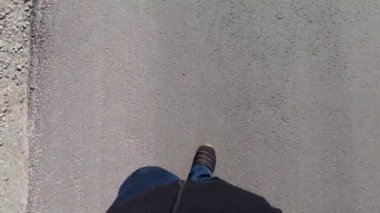 Bir adam asfalt yolda yürür. Erkeklerin ayakları asfaltta. Bir adam yol işaretleri boyunca yürür