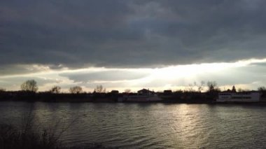 Nehirde gün batımı olan manzara. Bulutların arasından geçen güneş. Güneş ve su ışınları. Akşam yağmurlu manzarası.